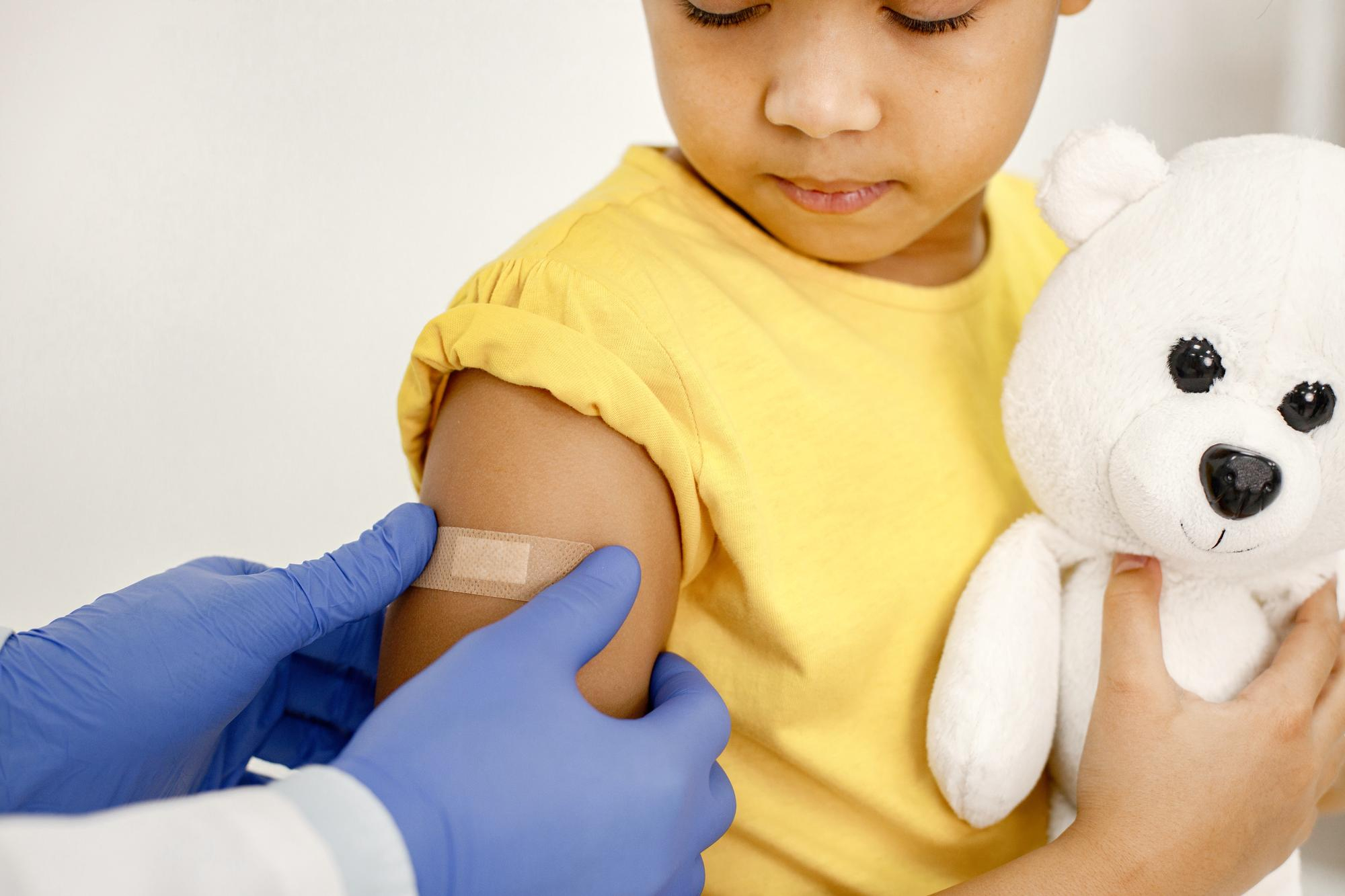 child holding stuffed animal having vaccine bandage placed on arm